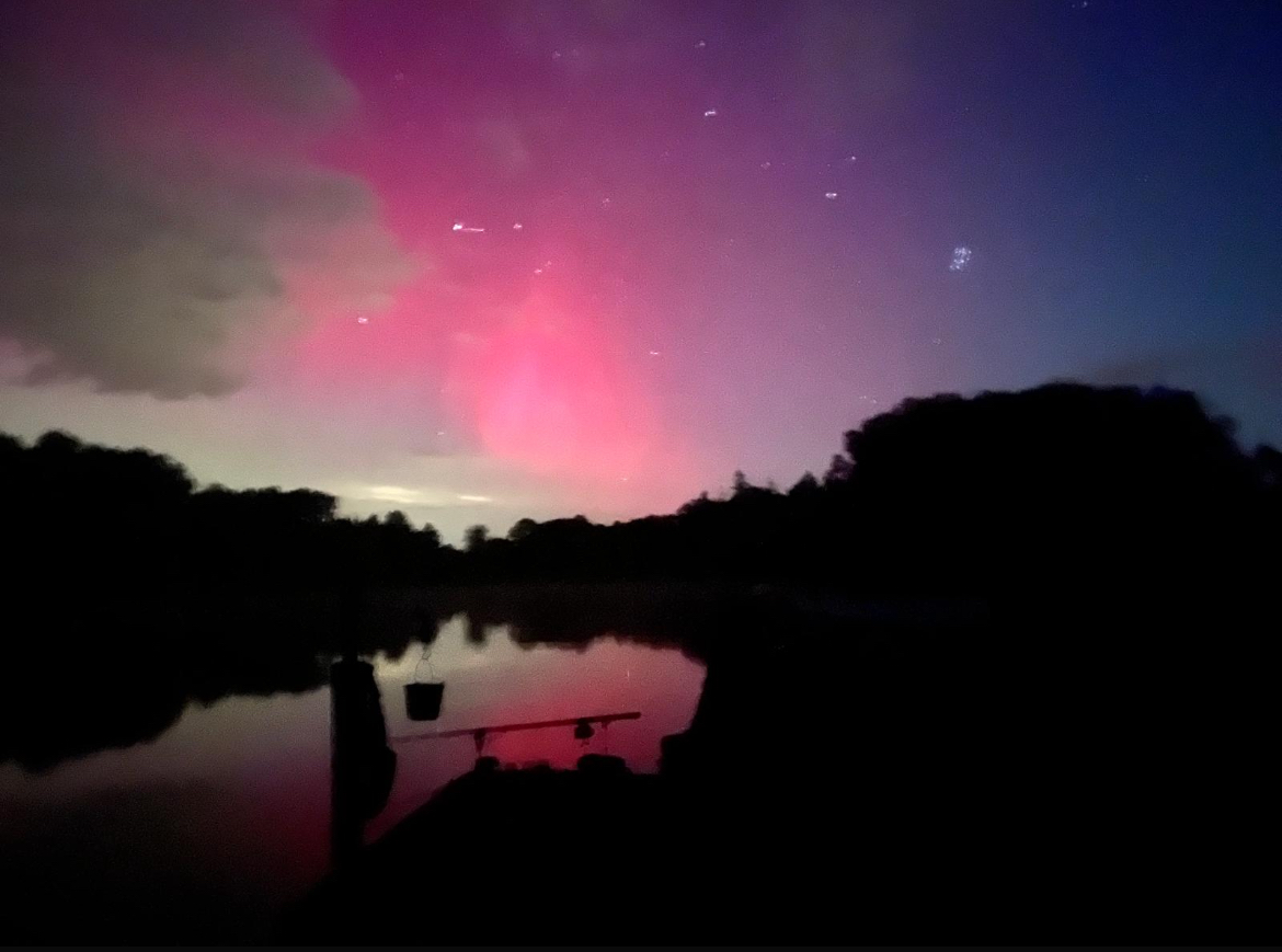 Northern lights (aurora borealis) glowing pink over the lake at Brittany Mill Lakes, rods set up in the foreground